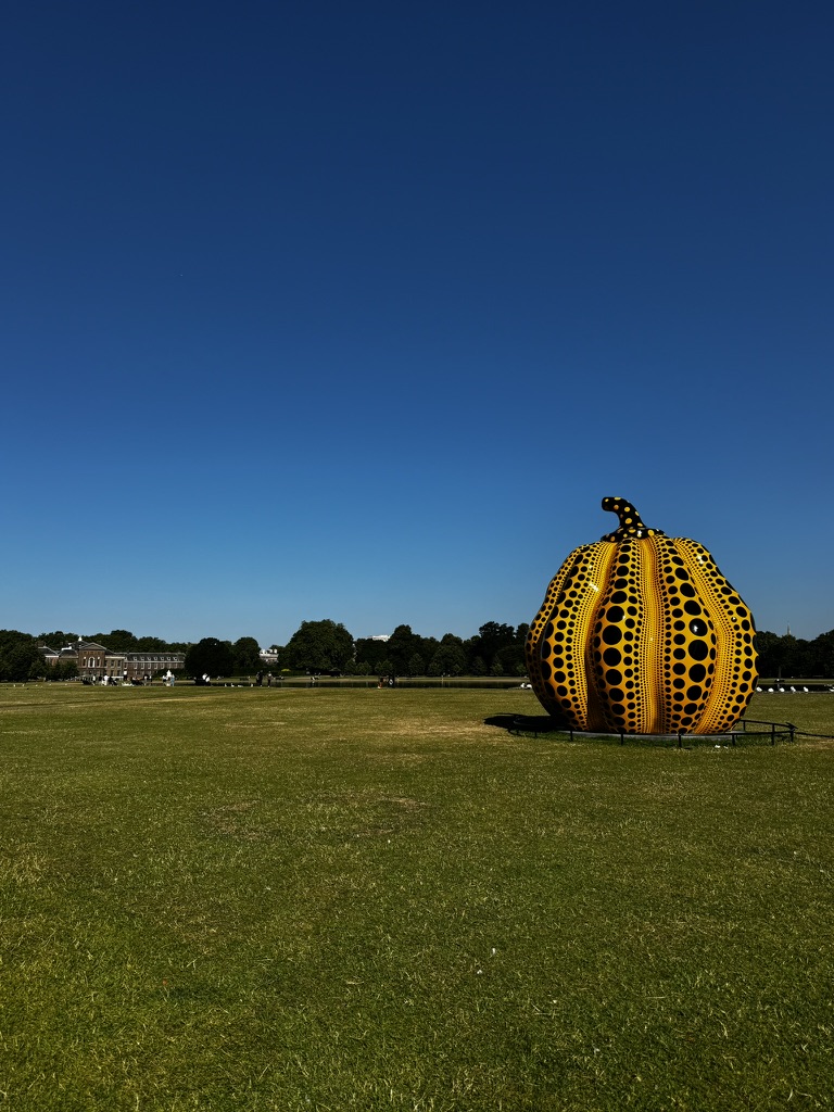 A famous Yayoi Kusama pumpkin sculpture in an open field, highlighting the exclusive "private art viewings" curated by Travellé.